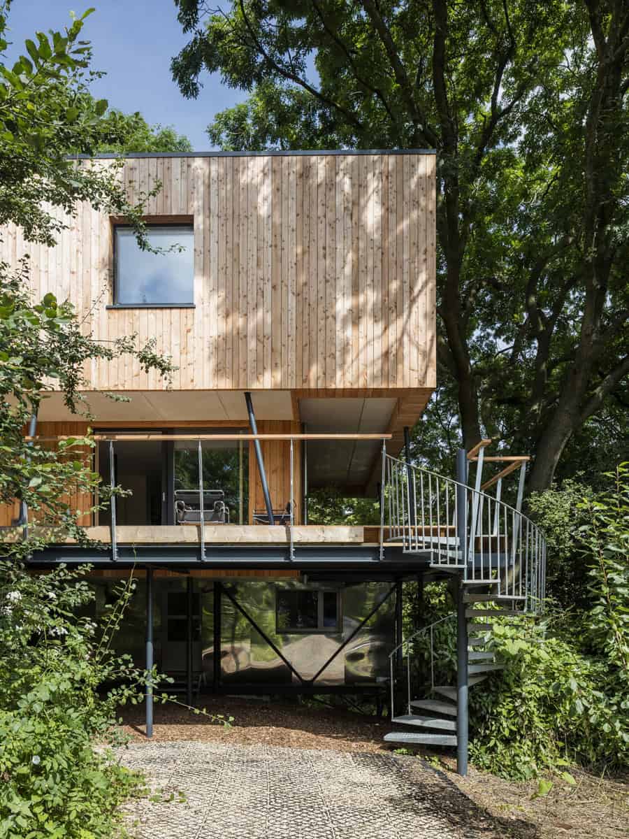 Dursley Treehouse timber-clad elevated home with steel stilts and spiral staircase among woodland, Gloucestershire